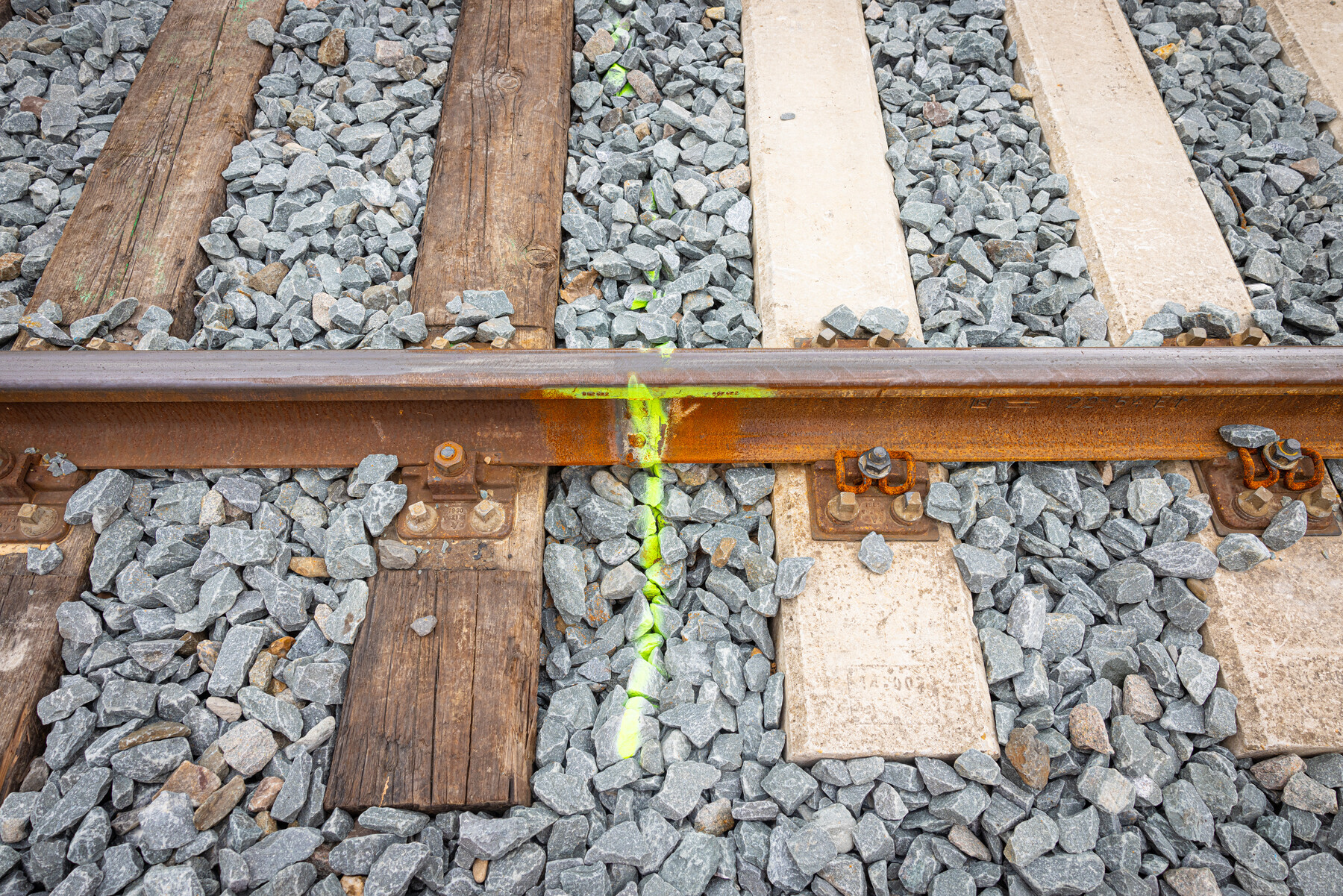 Het verschil tussen houten dwarsliggers links en betonnen dwarsliggers rechts. Het spoor wordt bij de gele streep doorgeslepen