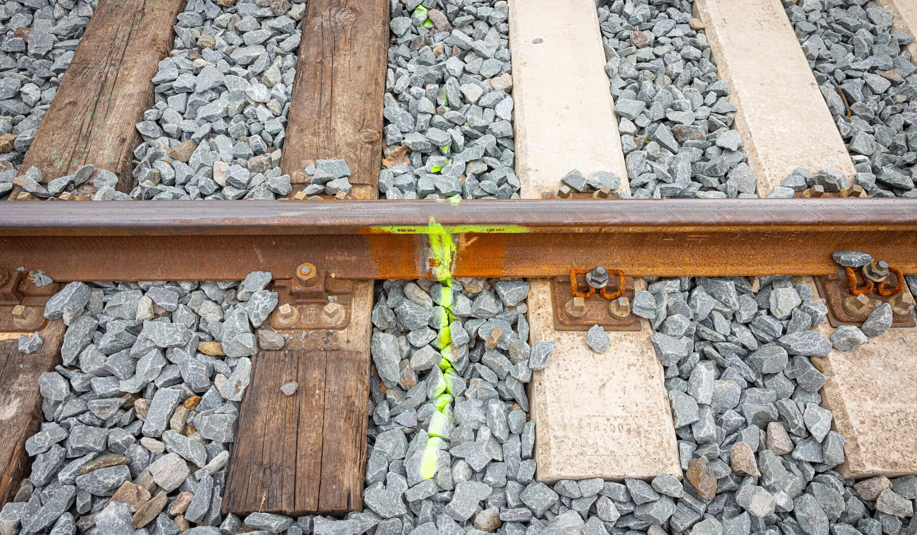Het verschil tussen houten dwarsliggers links en betonnen dwarsliggers rechts. Het spoor wordt bij de gele streep doorgeslepen