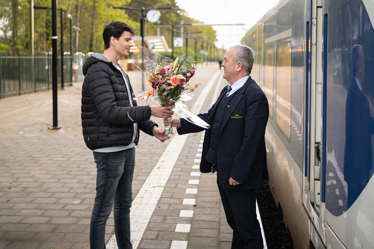 Projectmanager Arend Rook overhandigt bloemen aan de machinist van de eerste trein die weer stopte op het vernieuwde station