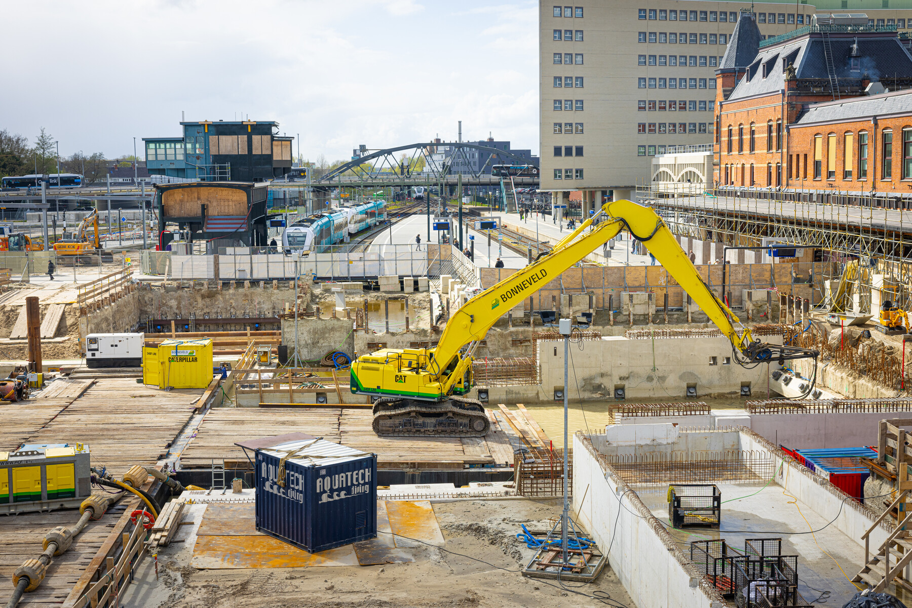 Een graafmachine staat op een drijvend ponton in de bouwkuip