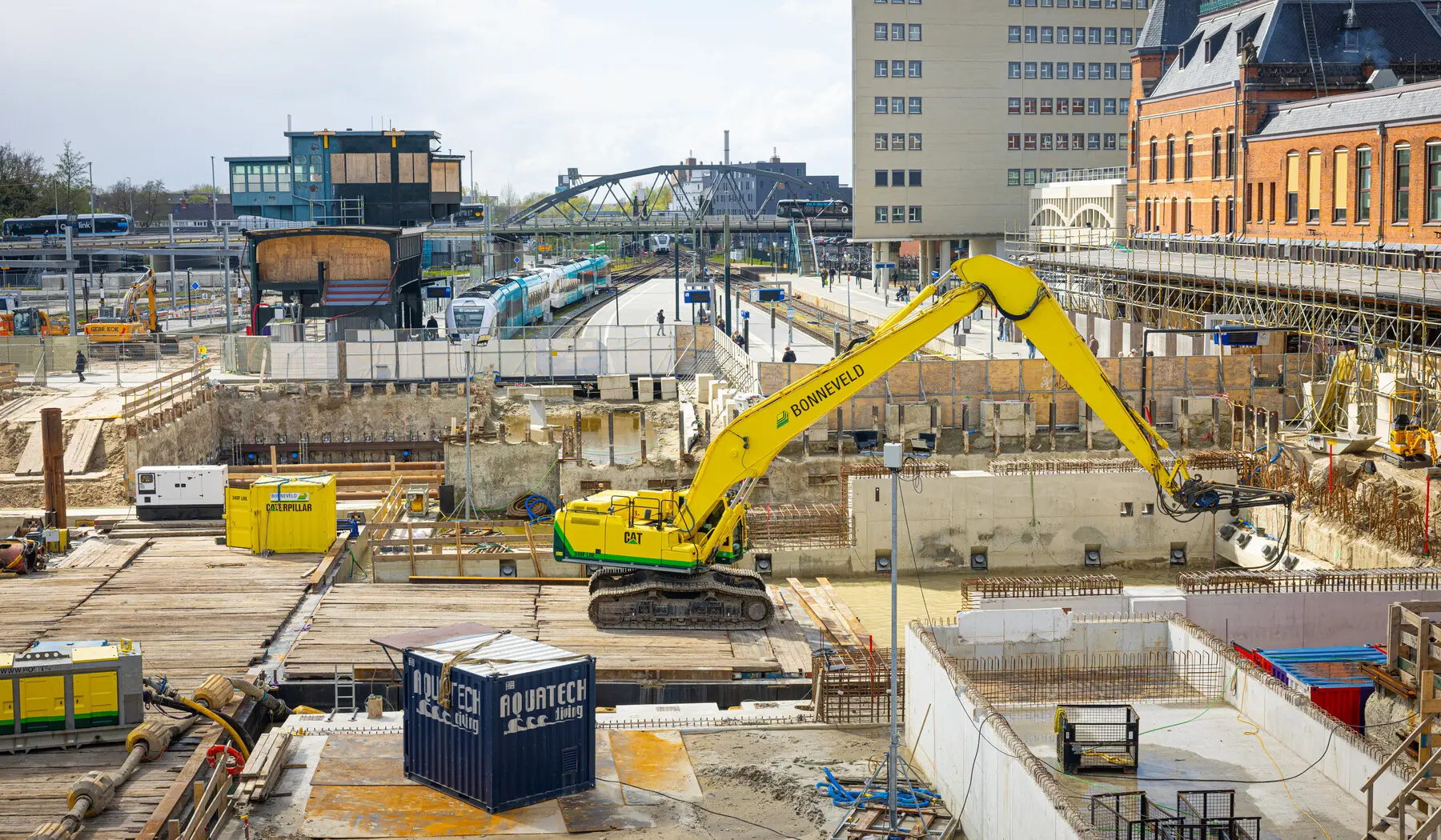 Een graafmachine staat op een drijvend ponton in de bouwkuip