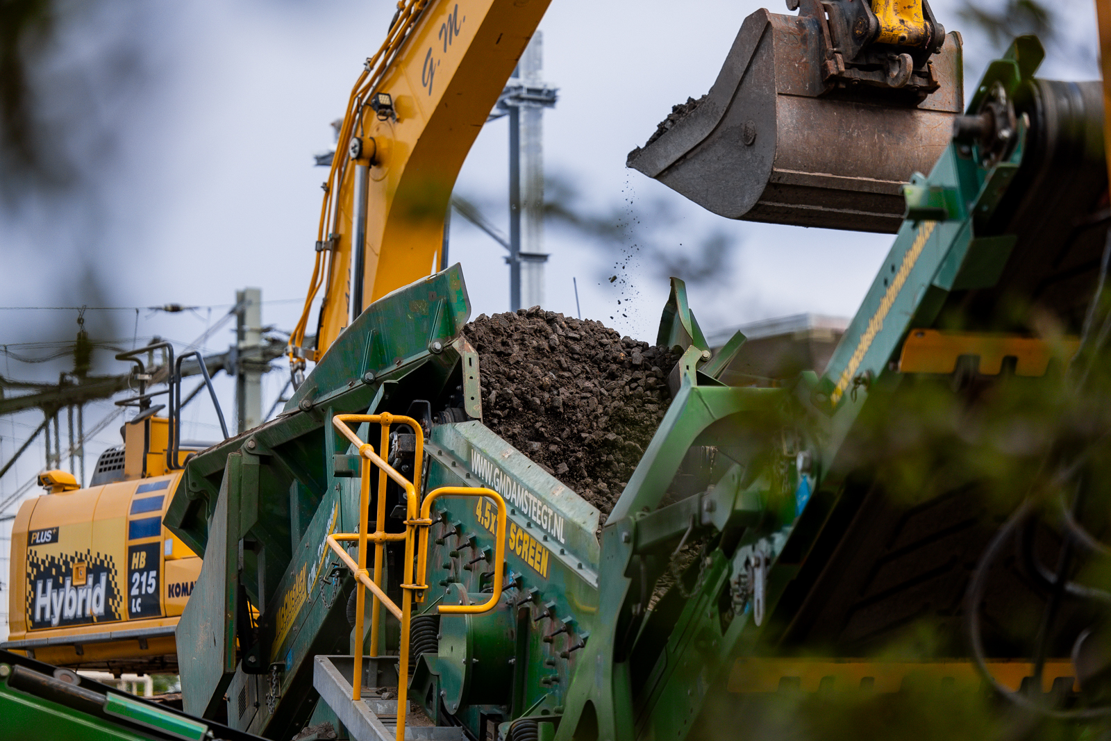 Een shovel werpt de oude ballast in de zeefinstallatie