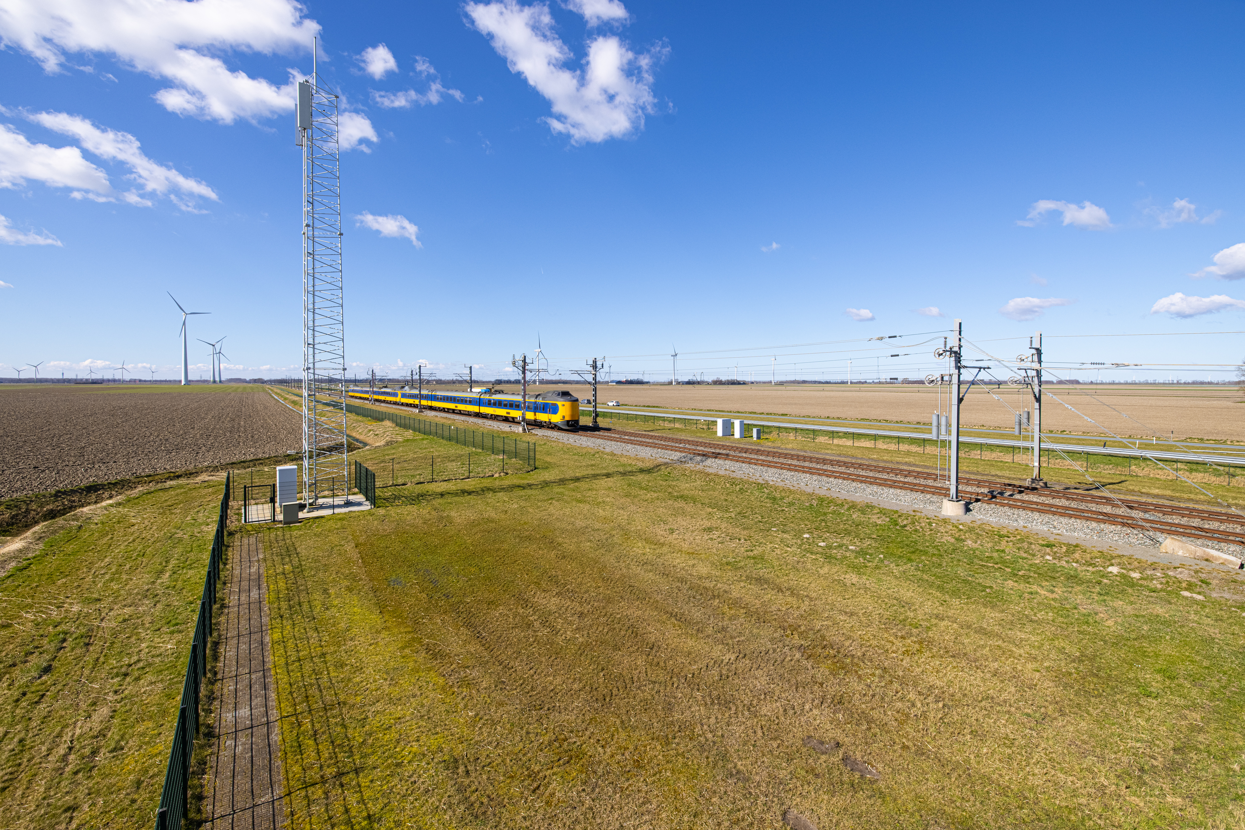 Een mast in het landschap naast het spoor