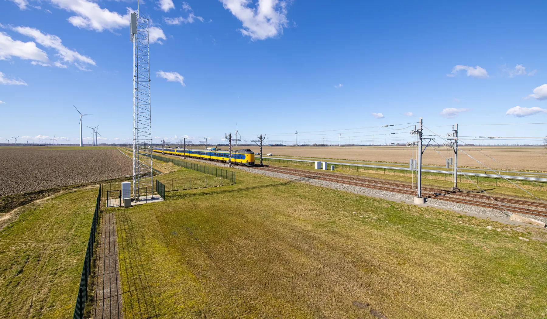Een mast in het landschap naast het spoor