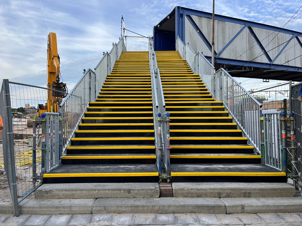 De nieuwe trap om de blauwe brug op te gaan die toegang geeft tot het station